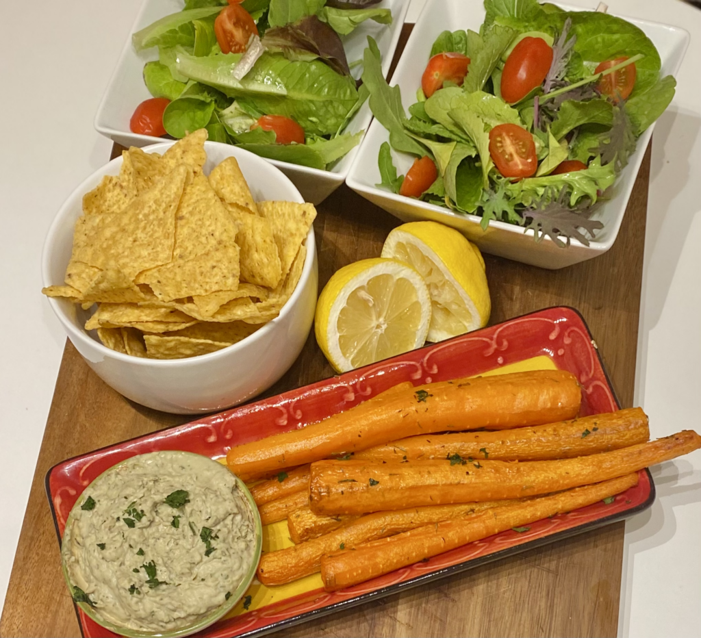 A tray of roasted carrots with hummus, chips and salad