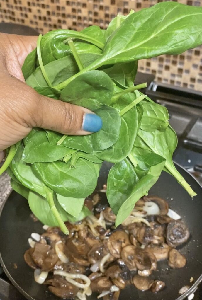 Handful of spinach going into pan with mushrooms and onions