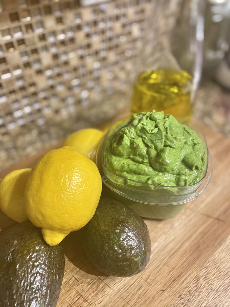 Bowl of Pesto surrounded by olive oil, lemons and avocados.