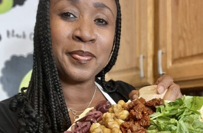 woman holding cutting board topped with hummus, roasted chickpeas, olives, sundried tomatoes and spinach