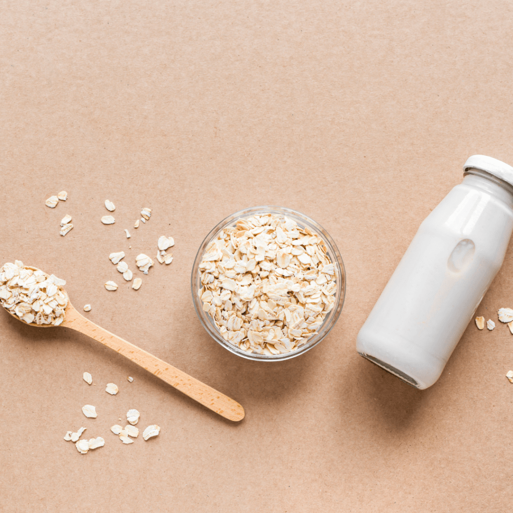 Rolled oats in a bowl and on a spoon next to a bottle of oat milk