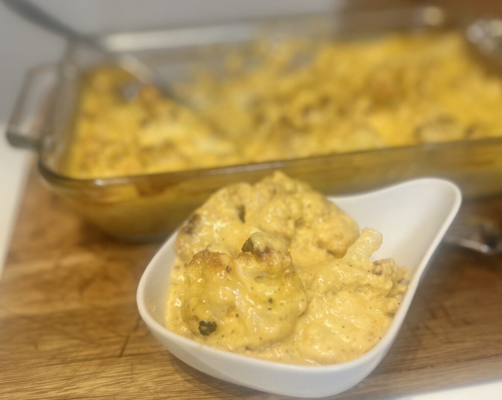 Bowl of cauliflower "mac" and cheese in front of a fresh baked dish of cauliflower "mac" and cheese