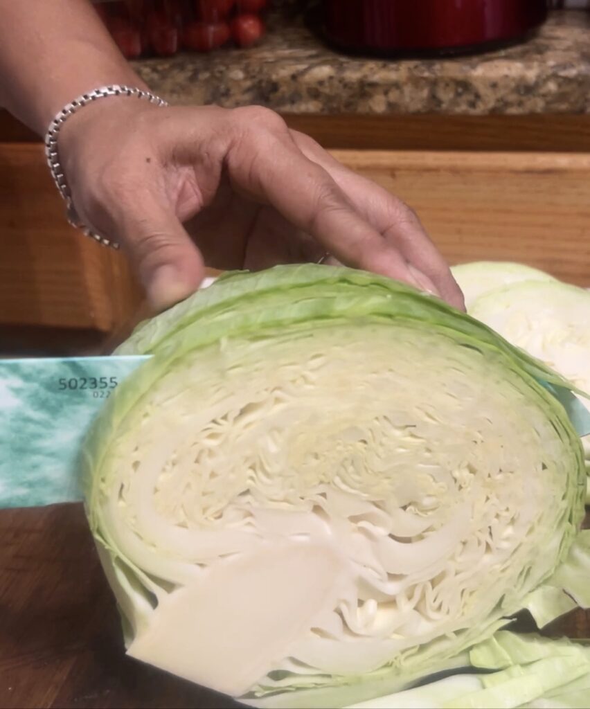 Head of green cabbage being sliced with a turquoise green chef's knife

