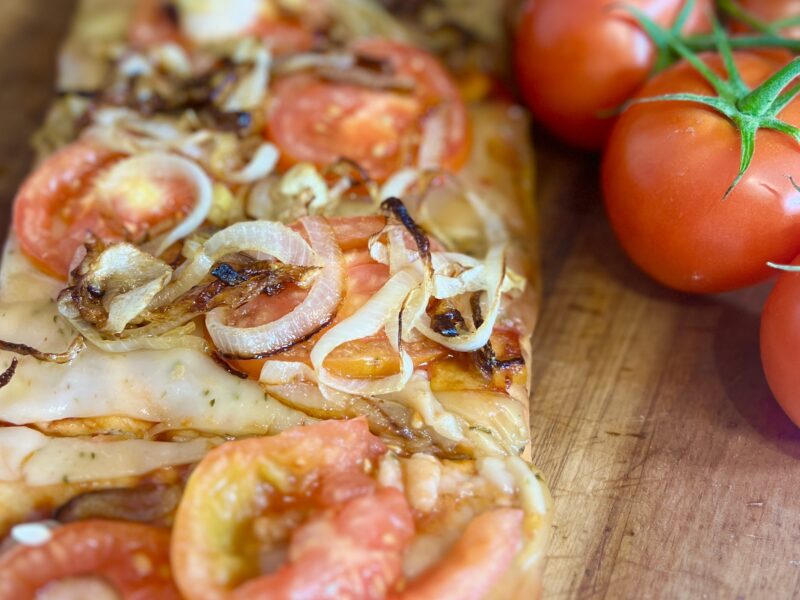 Flatbread pizza with tomato and caramelized onions on a cutting board next to fresh tomatoes on the vine.