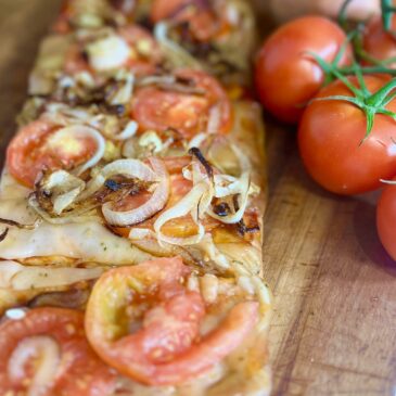 Flatbread pizza with tomato and caramelized onions on a cutting board next to fresh tomatoes on the vine.