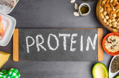 The words "PROTEIN" on a black chalkboard surrounded by lentils, vegetables and seafood