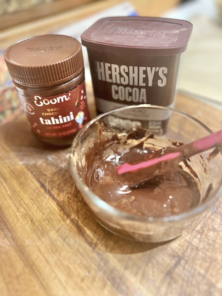 Jar of chocolate hummus next to cocoa powder and a bowl of chocolate hummus