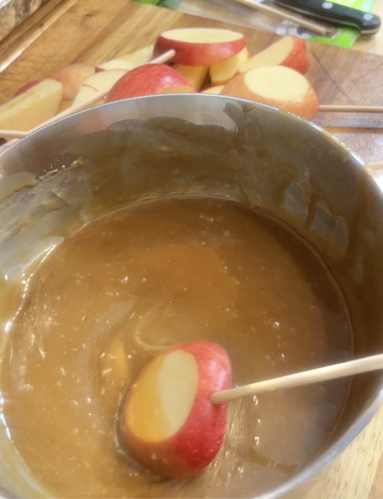 A slice of apple on a stick swirling in the sauce to create a vegan caramel apple