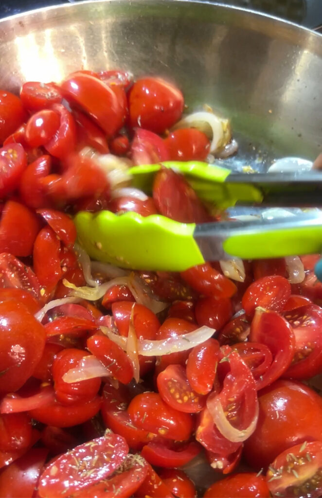 cherry tomatoes with onions in pan being tosse with green tongs
