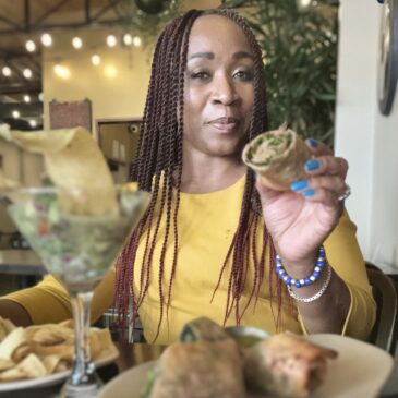 African american woman with braids holding a tex egg roll in her hand with a martini glass filled with coconut ceviche in front of her