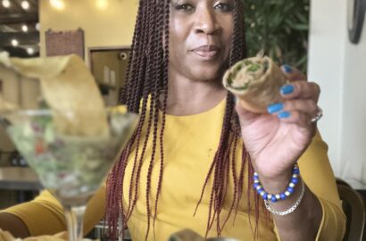 African american woman with braids holding a tex egg roll in her hand with a martini glass filled with coconut ceviche in front of her