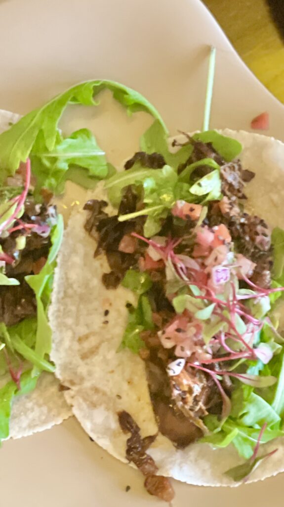 BBQ Korean Tacos: Soft cassava taco topped with microgreens, mushrooms, tomatoes and cilantro and tossed in bbq sauce