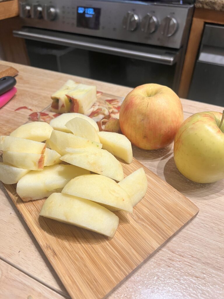 Sliced apples on a cutting board are one ingredient in a sheet pan dinner