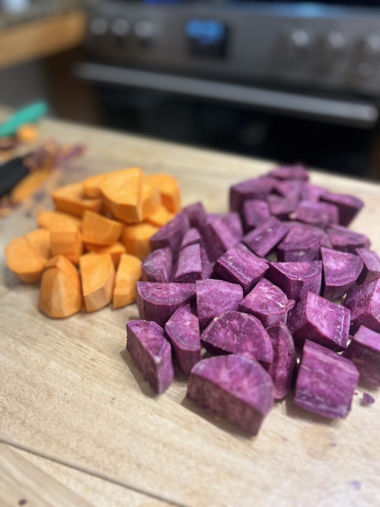 sweet potatoes and purple purple sweet potatoes are prepared on a cutting board for this sheet pan dinner